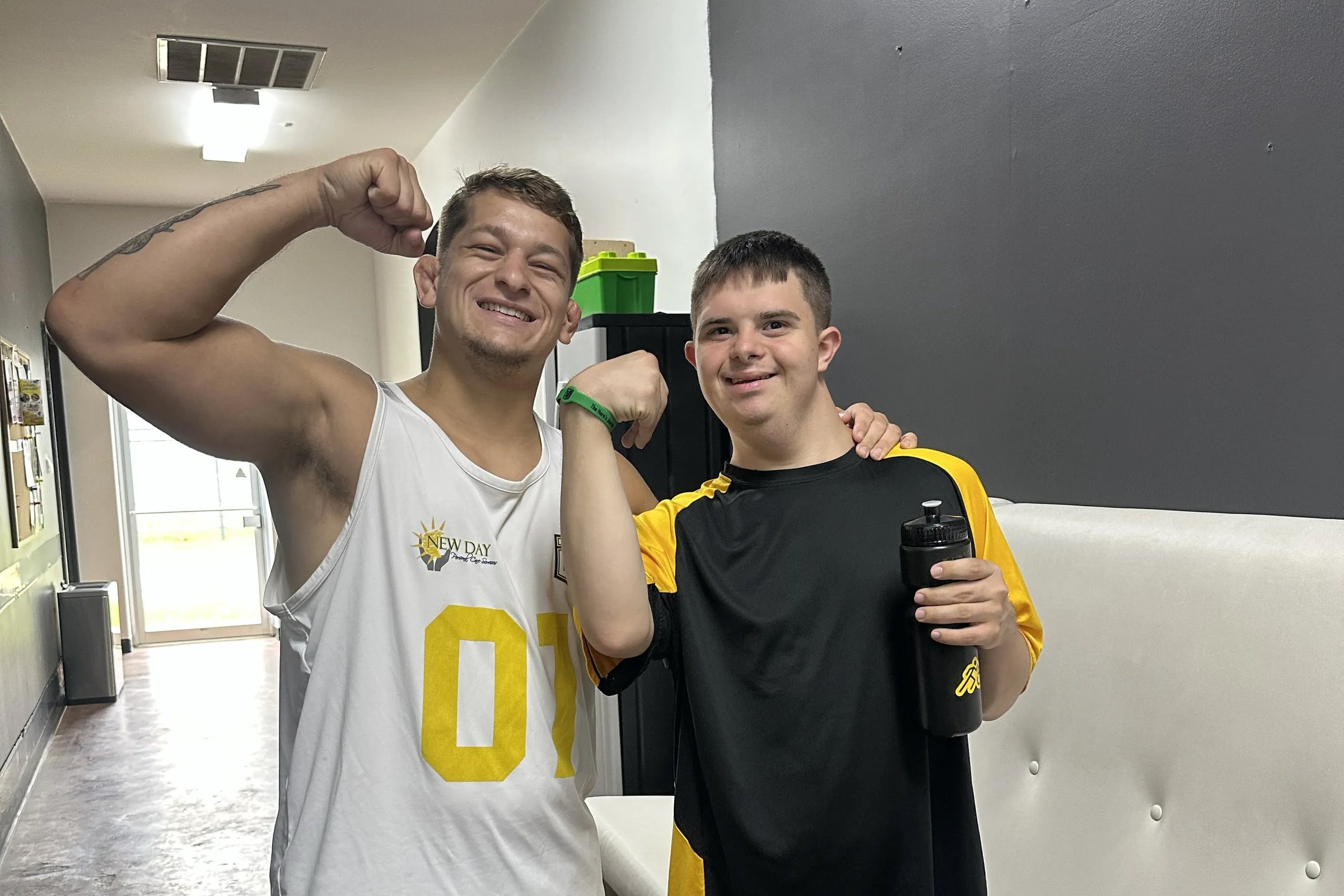 A coach in a white jersey and an athlete in a black-and-yellow Train Unique jersey flex side by side, both grinning