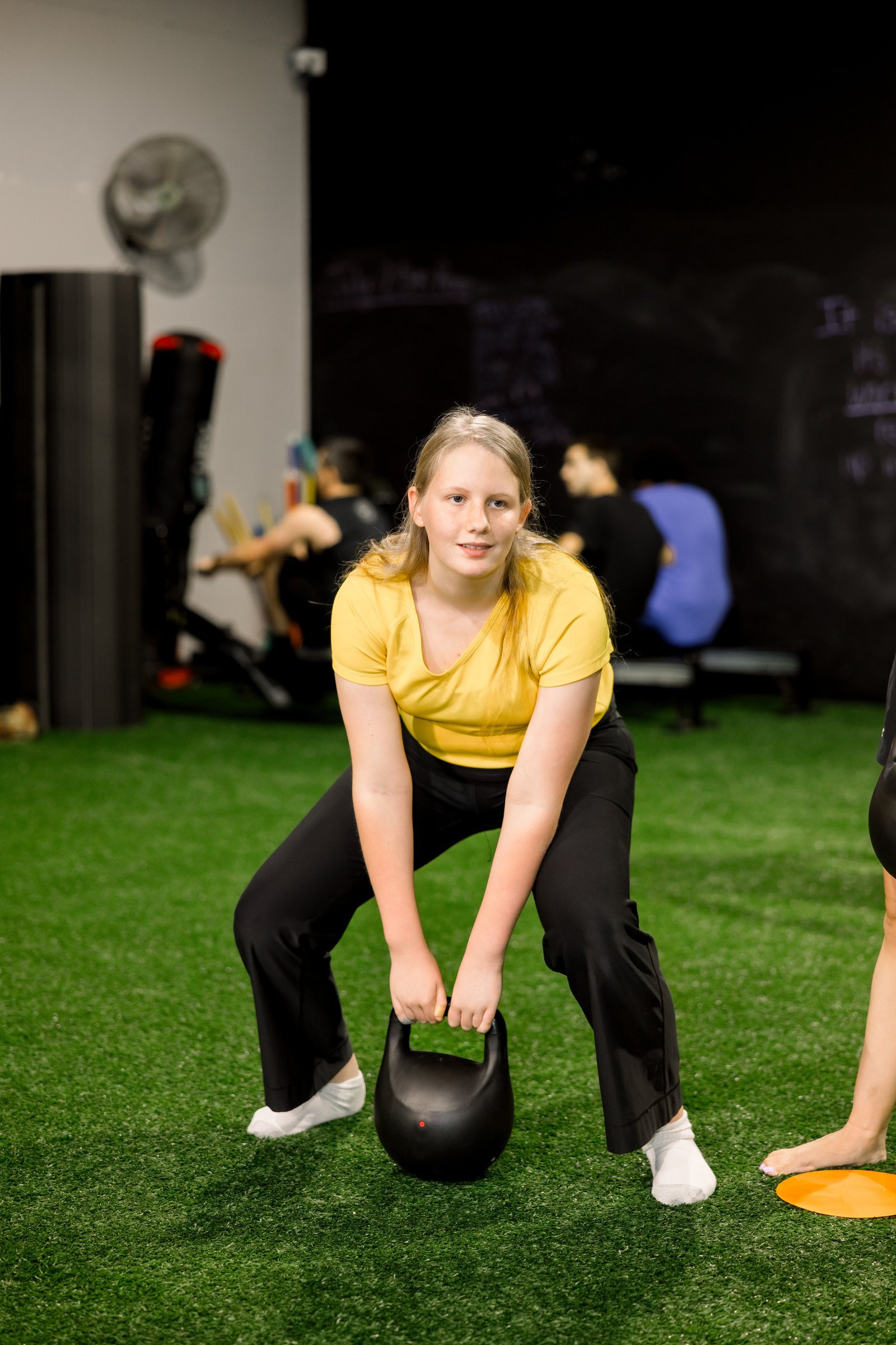 A young athlete setting up her kettlebell deadlift on the turf